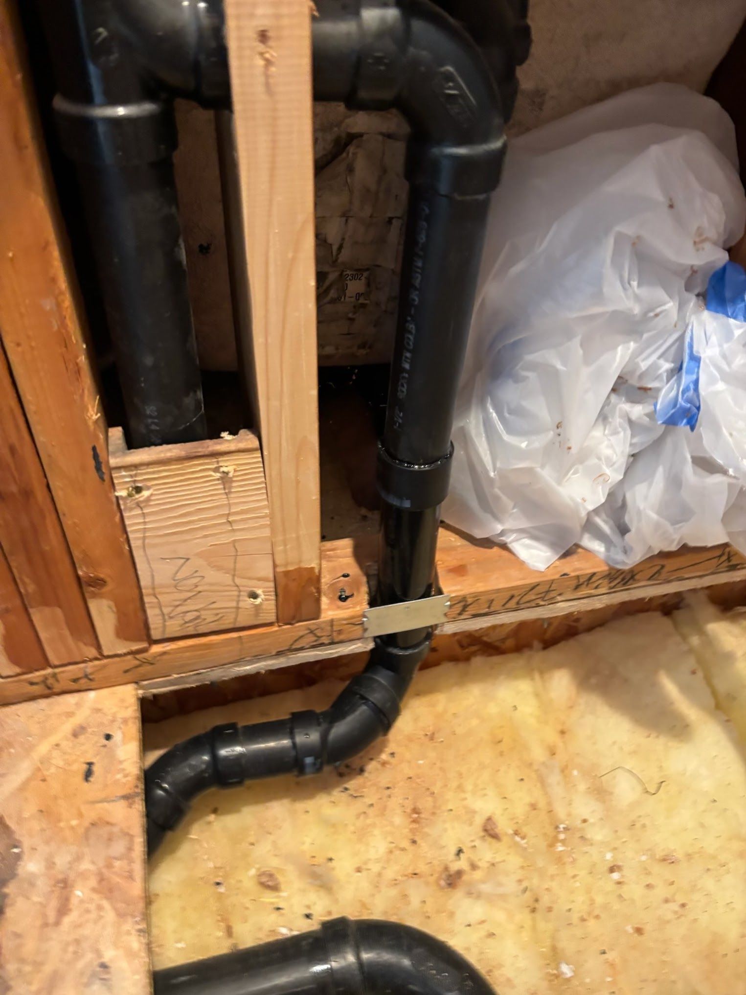 Black plumbing pipes in a wooden frame; pipes snake along floor.  Insulation and a plastic bag are also visible.