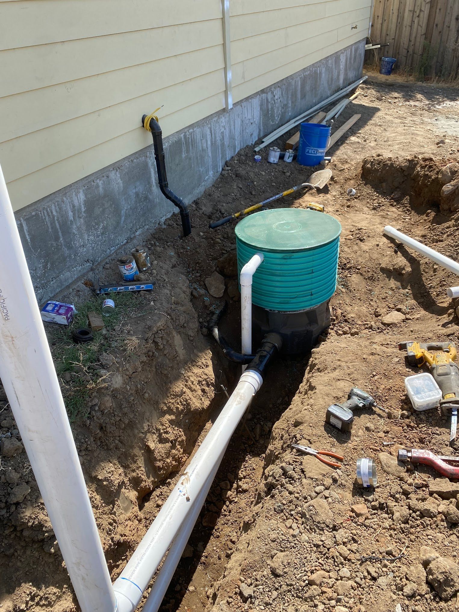 Installation of a residential drainage system. White PVC pipes, a green tank, and black co