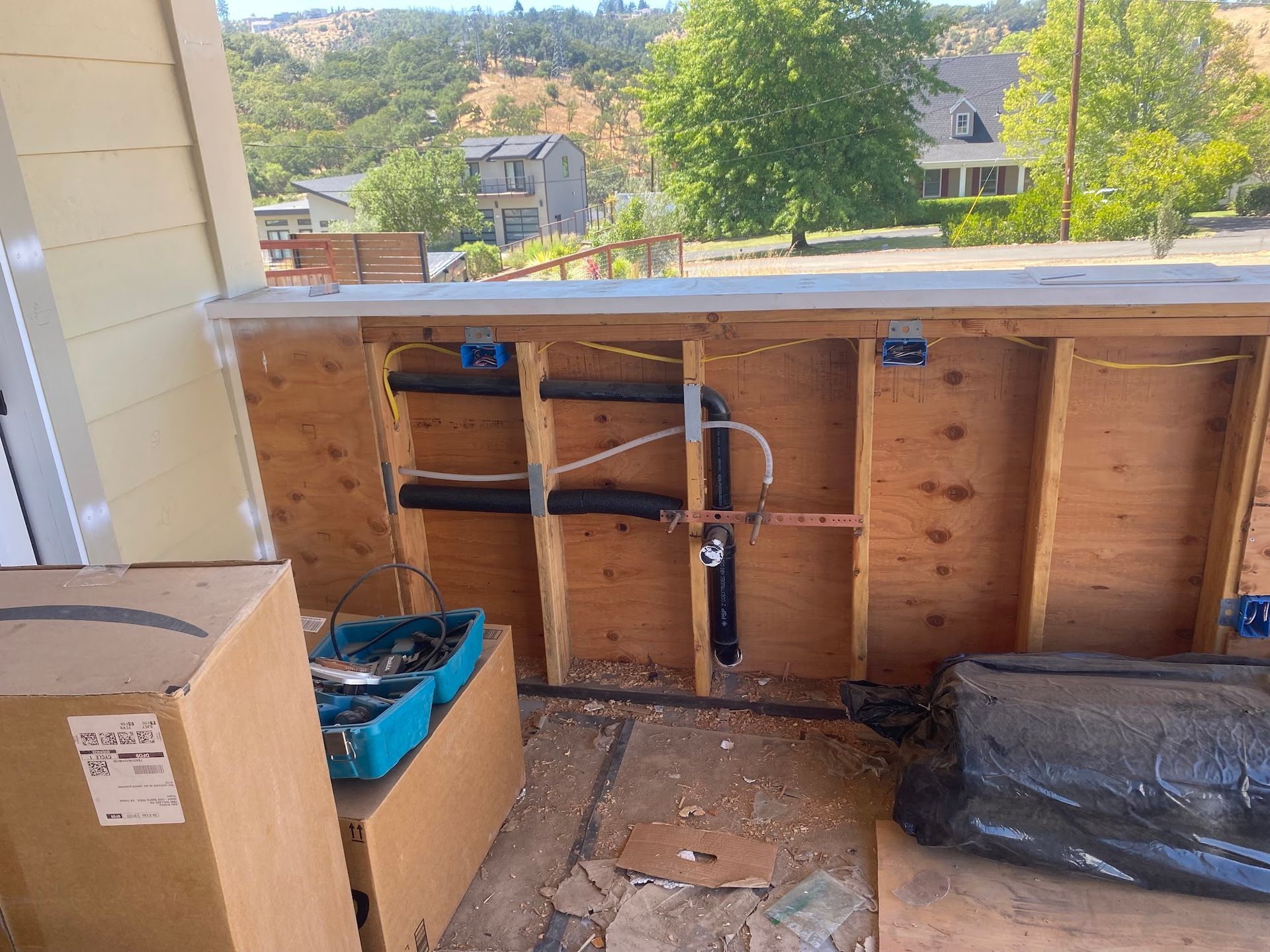 Construction site. Exposed pipes and wiring within wooden wall. Outdoors, sunny day.