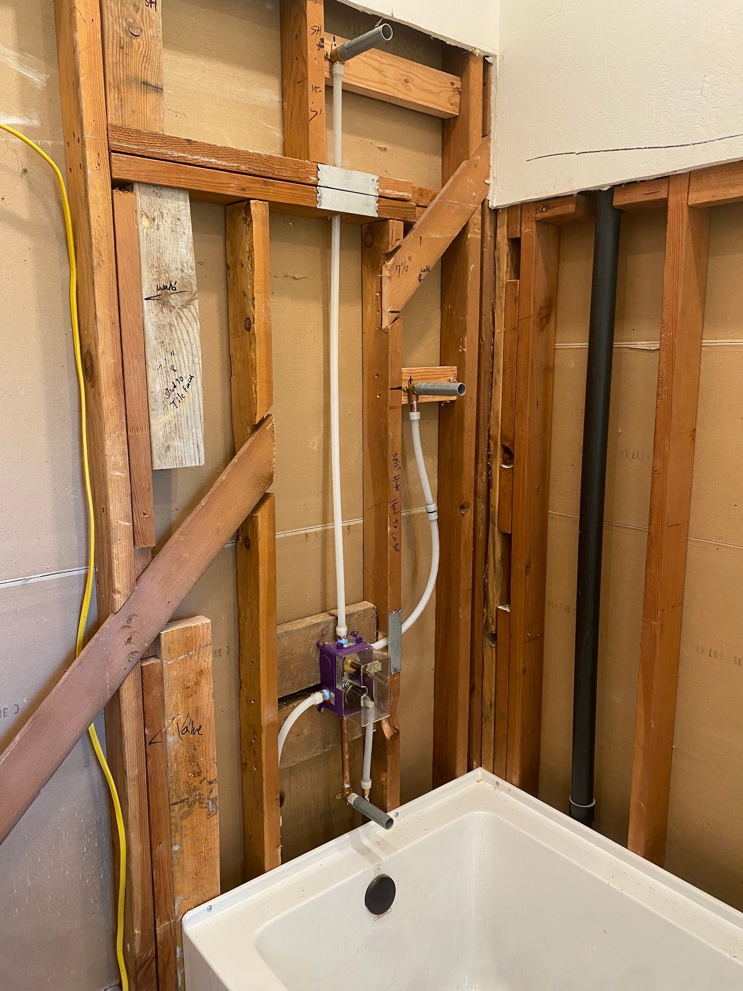 Bathroom under renovation, showing exposed framing, plumbing, and bathtub.