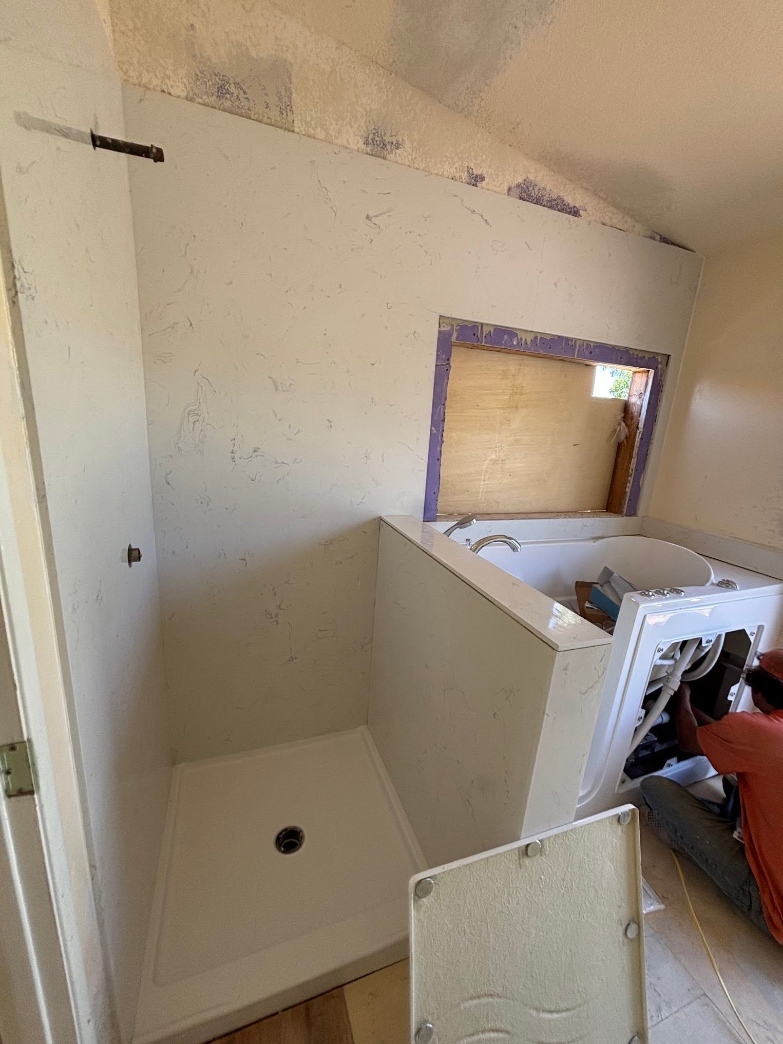 Bathroom renovation: shower stall and bathtub alcove under construction. White walls, unfinished wood.