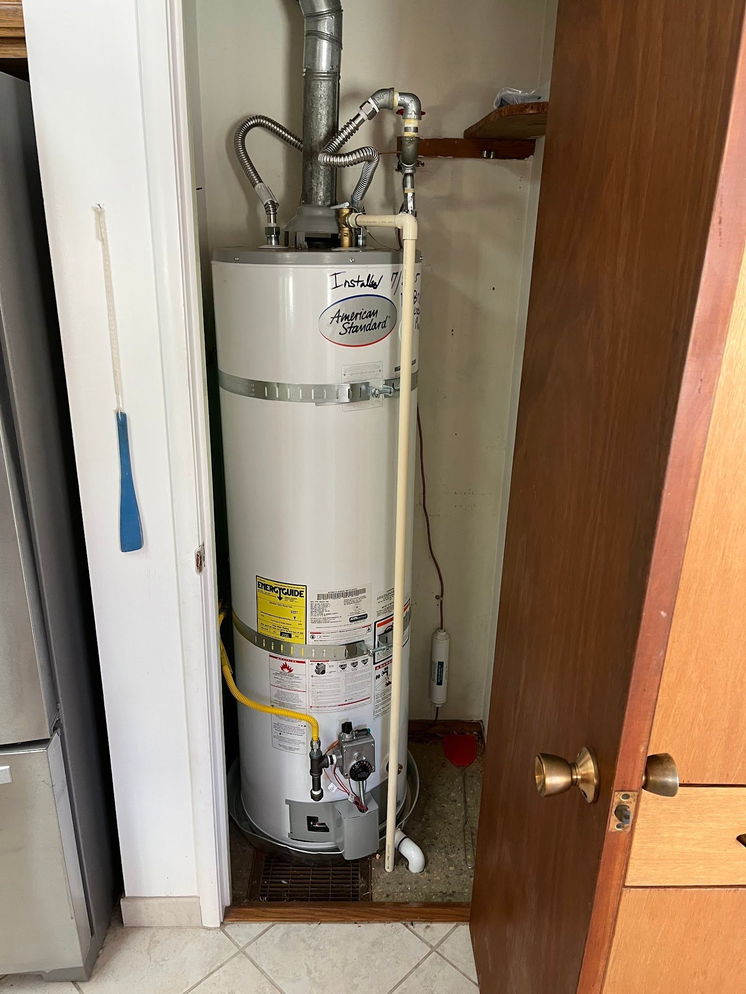 A white water heater inside a closet with a door open, next to a refrigerator.
