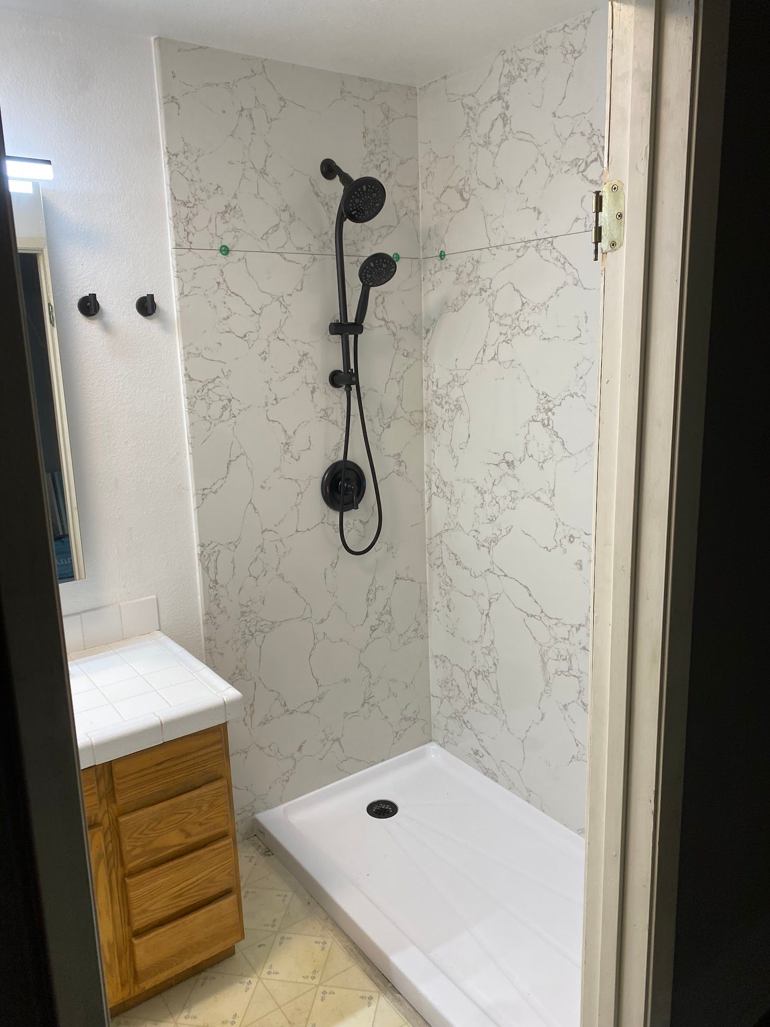 Bathroom with marble-patterned shower walls, black fixtures, and a white shower base. Light wood vanity to the left.