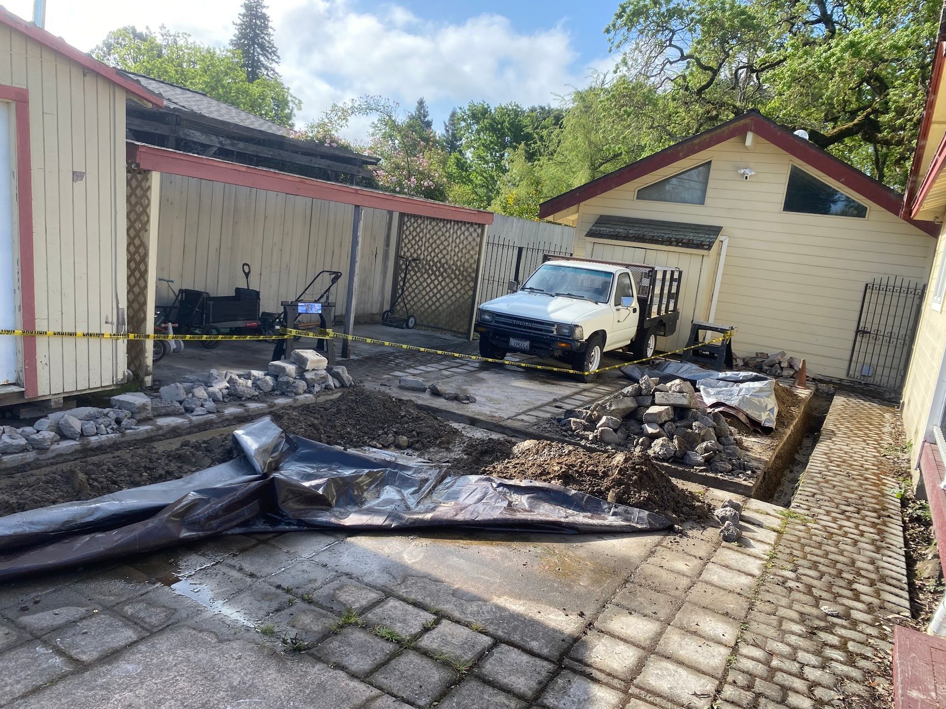 Yard with construction debris: white truck, gravel, yellow tape, and buildings with tan and white exteriors.