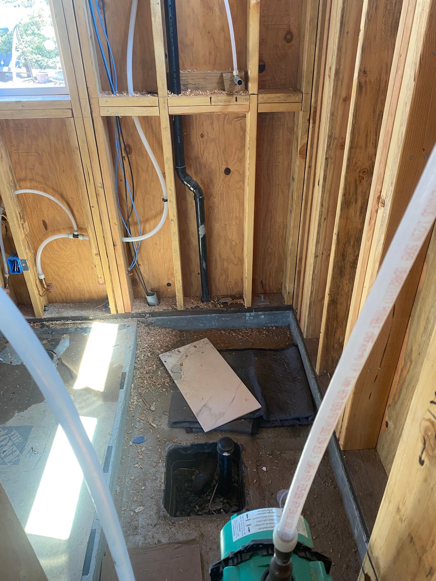 Interior view of a construction site with exposed wooden framing and plumbing. White pipes and black drainage.