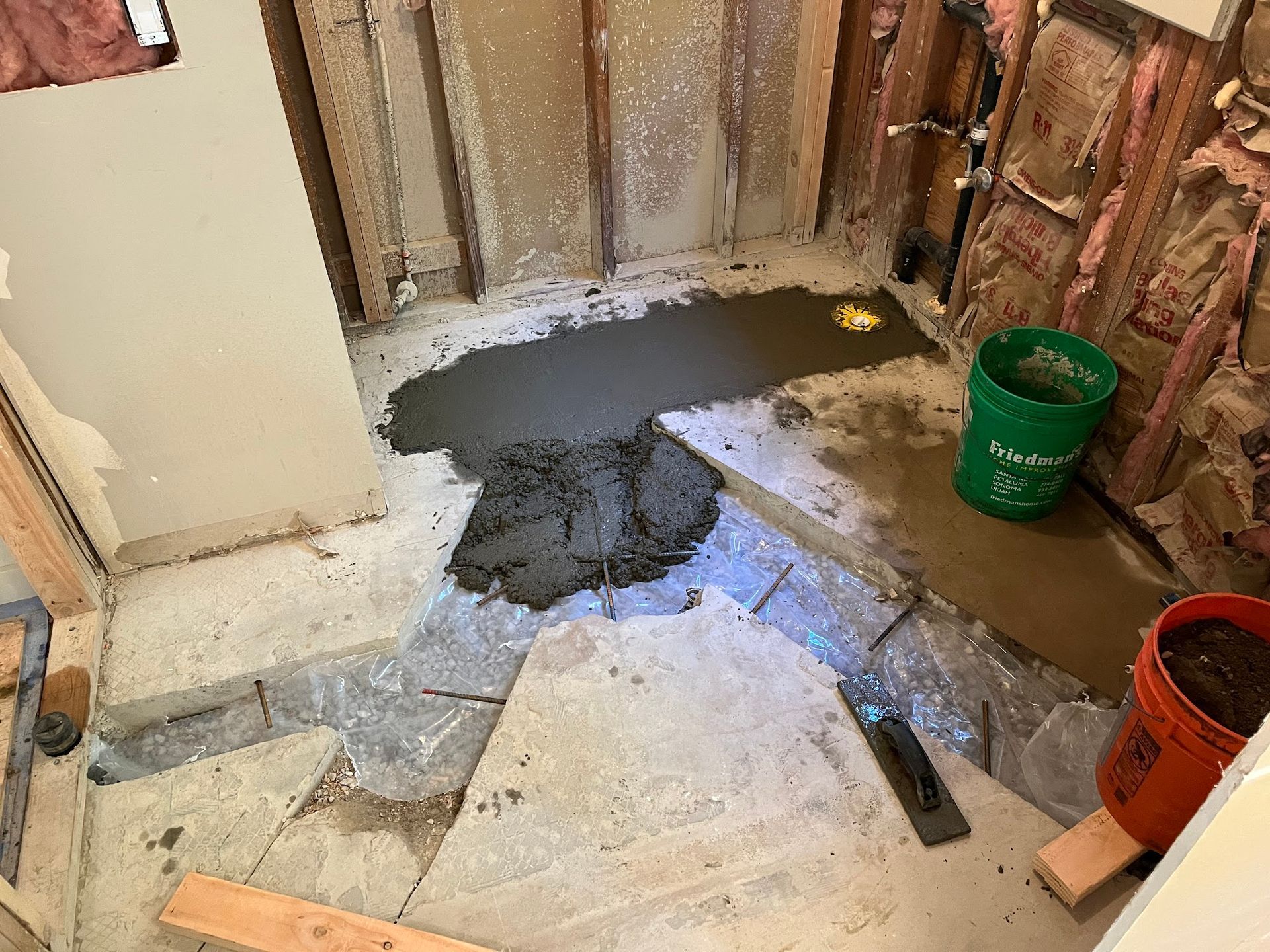 Bathroom remodel: Wet cement poured in the shower pan, framing visible. Buckets and tools nearby.