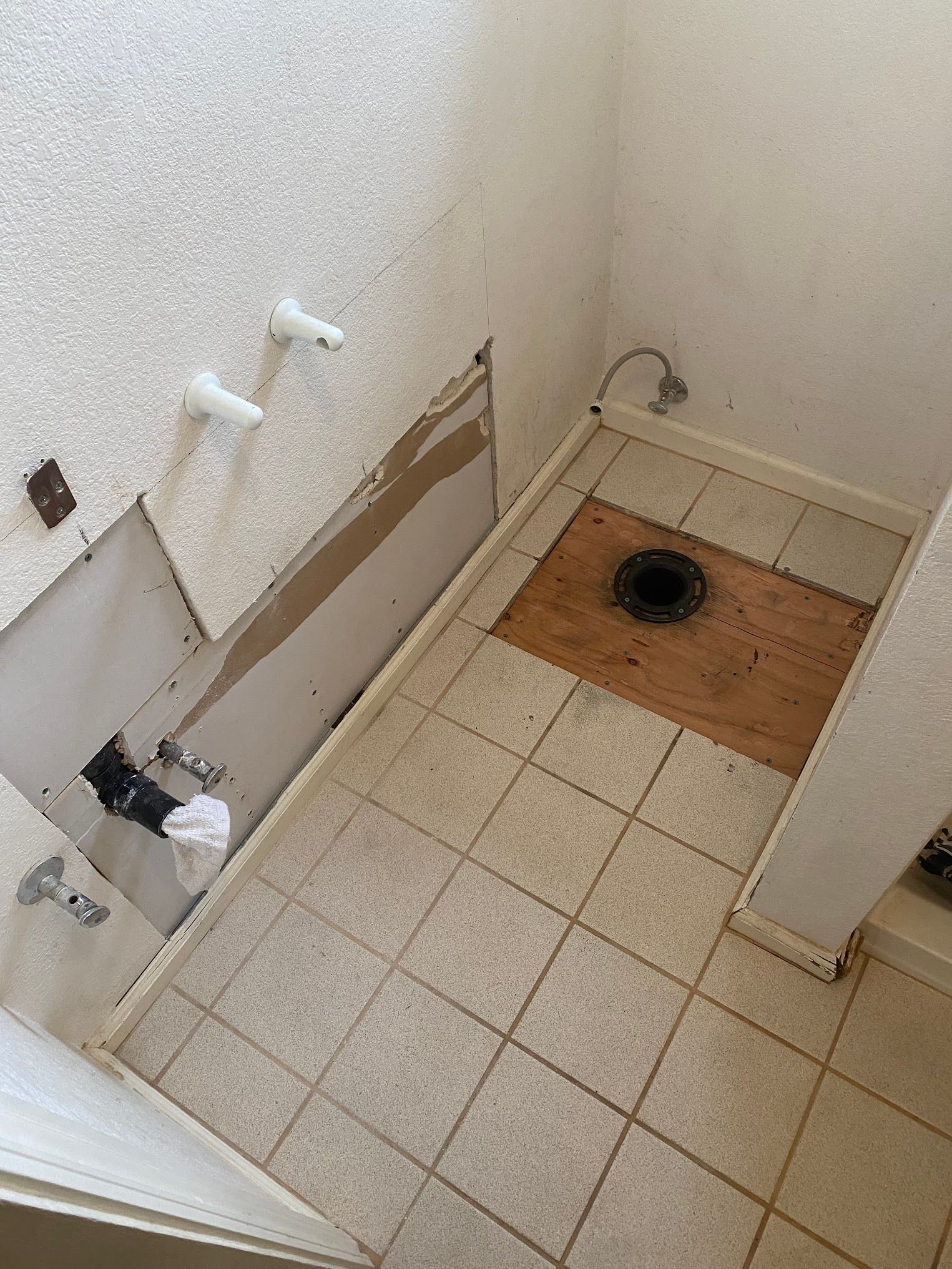 Bathroom under construction; exposed plumbing, damaged walls, tile floor, and sink fixtures.