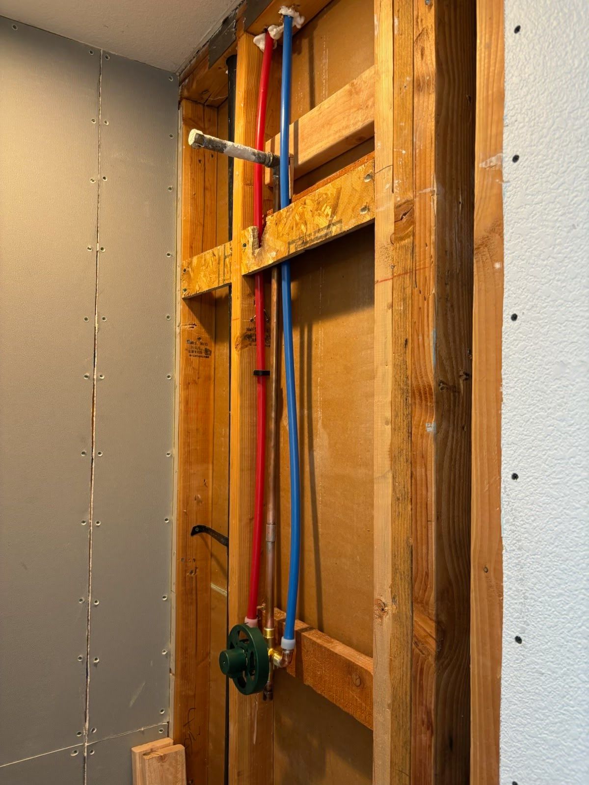 Bathroom plumbing installation in a wooden wall. Red and blue pipes with showerhead fixture.