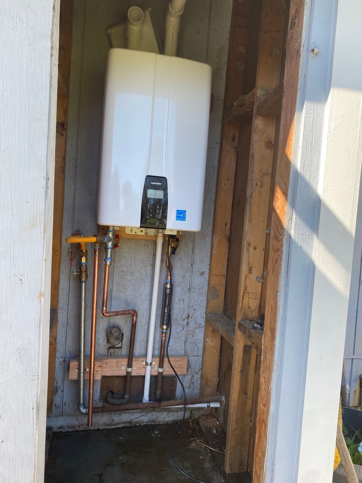 Tankless water heater mounted in a wall alcove with copper piping.