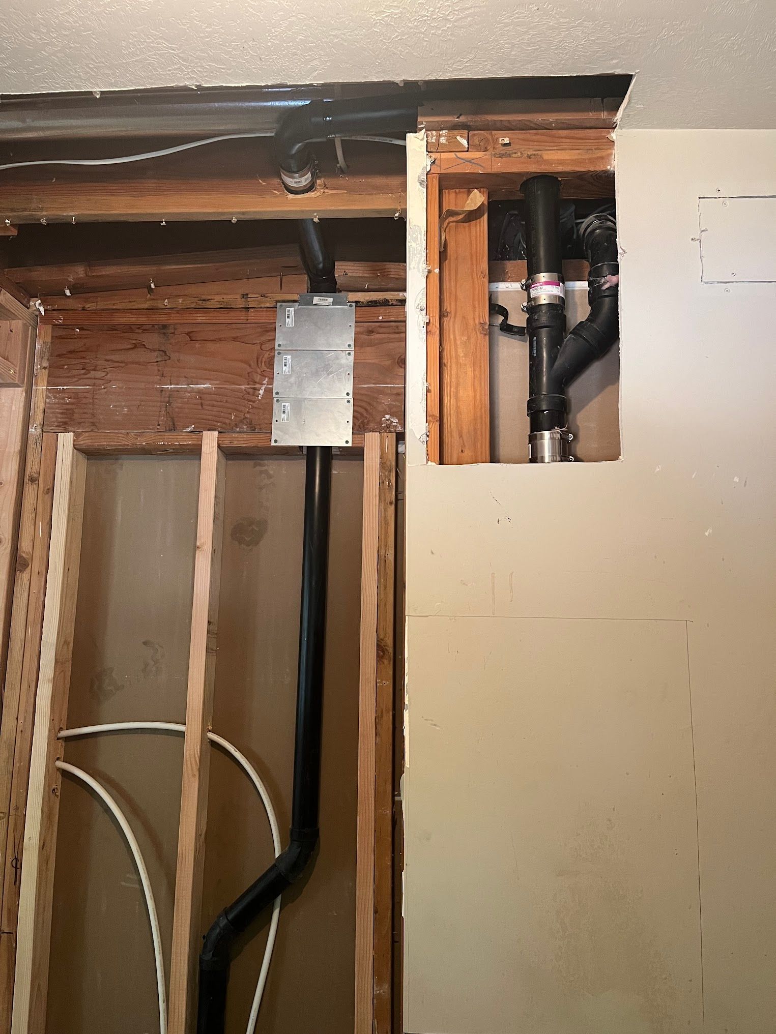 Wall with exposed plumbing and electrical conduit. Studs, pipes, and electrical box visible during renovation.