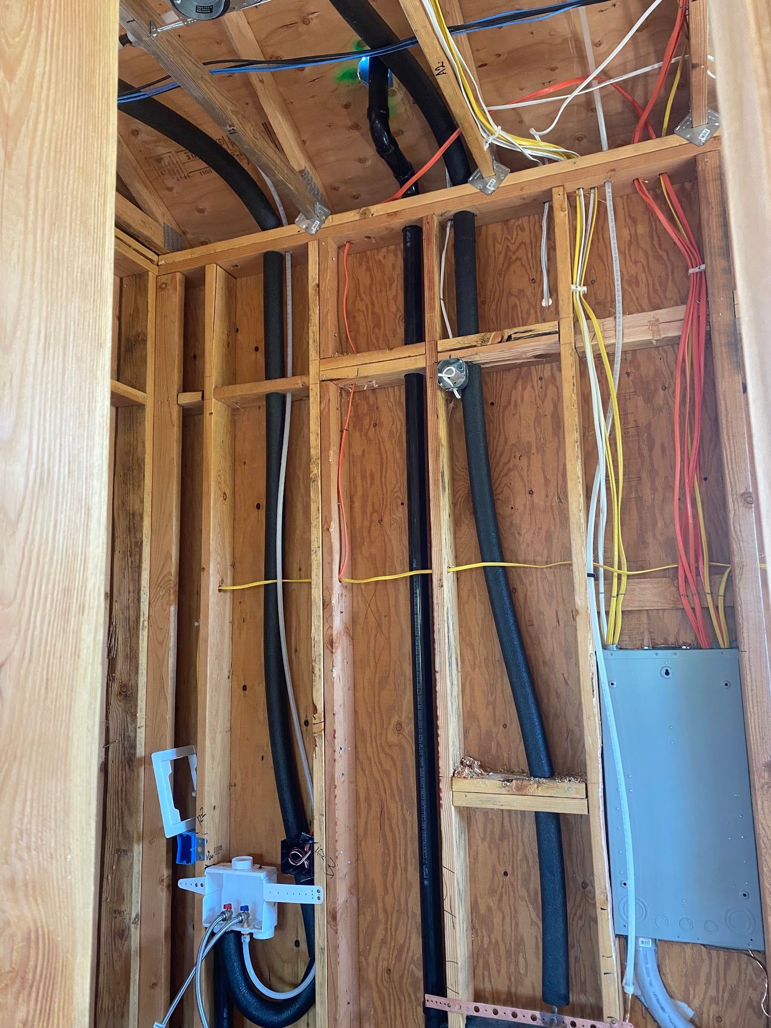 Wooden wall with electrical wiring and conduit, gray electrical panel visible.