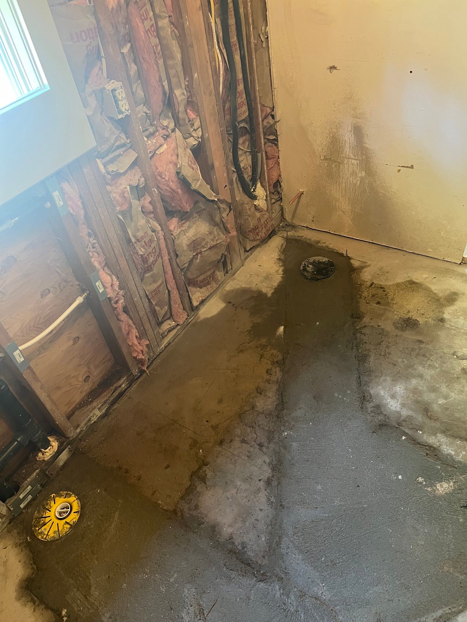 Water damage in a room: exposed wall studs, soaked floor, and a yellow drain.