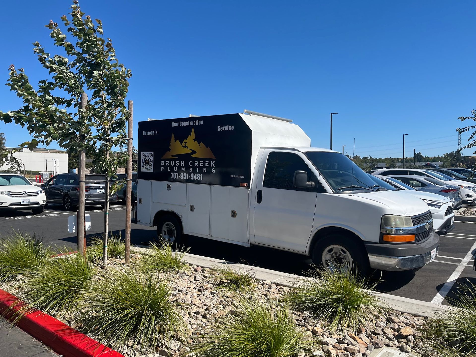 White work truck in a parking lot, with a company logo on the side, on a sunny day.
