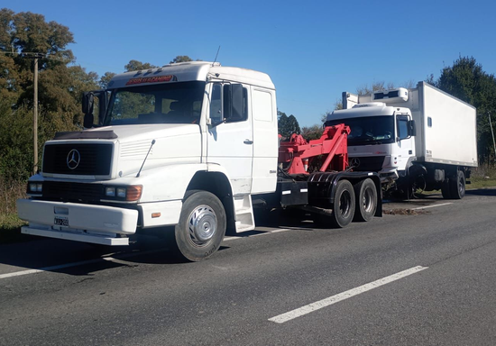 Una grúa remolcando un camión blanco en una autopista bajo un cielo azul despejado.