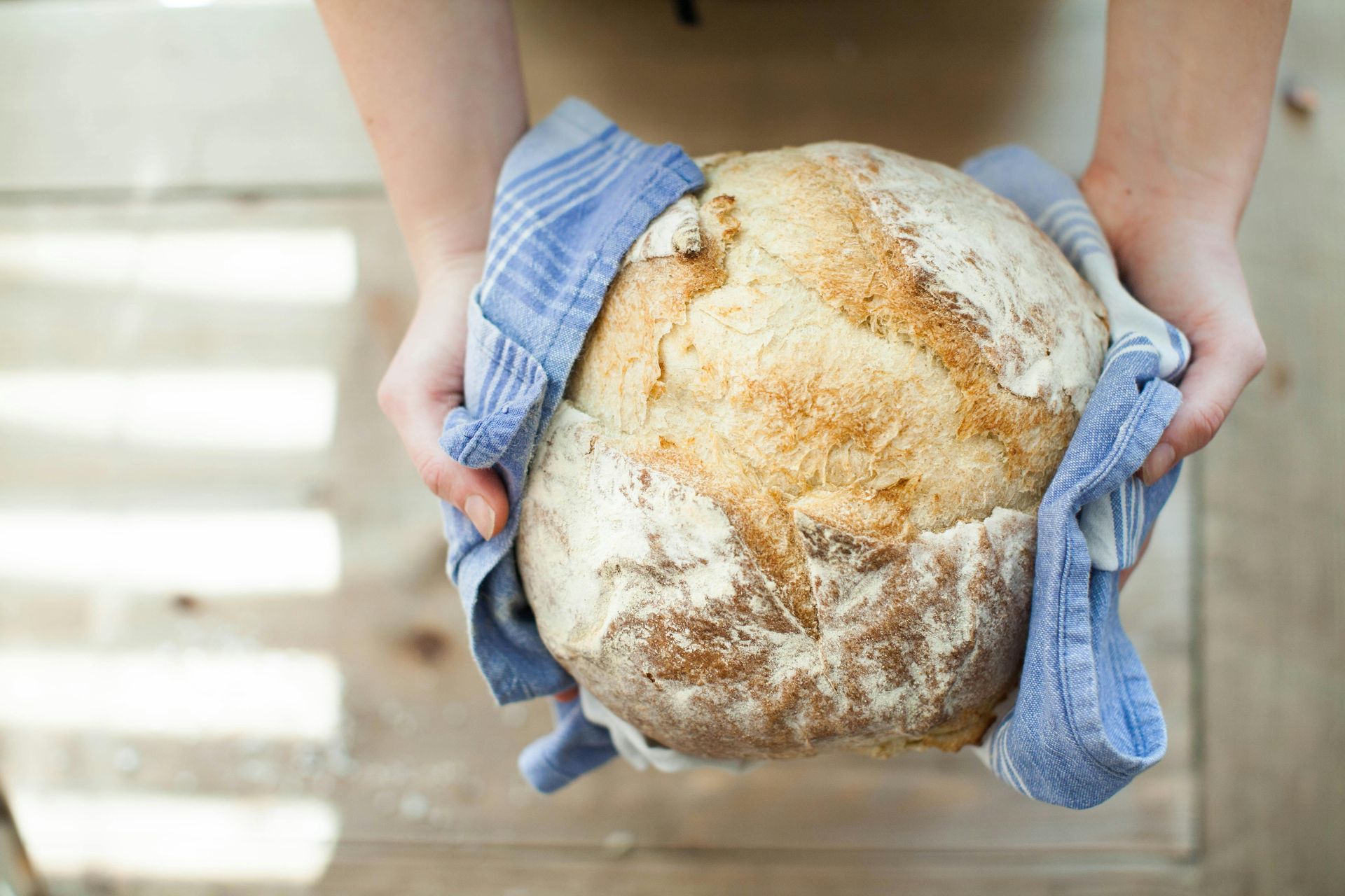A person is holding a loaf of bread wrapped in a blue towel.