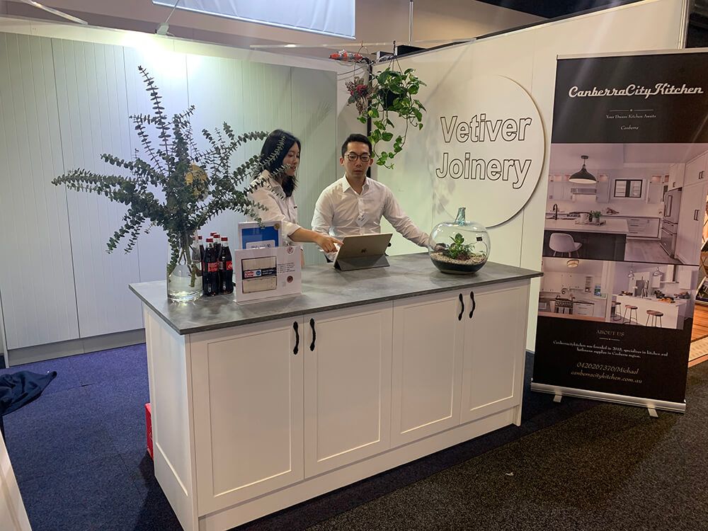 A Man and A Woman Are Standing at A Counter in Front of A Sign — Canberra Kitchen & Bathroom in Fyshwick, ACT