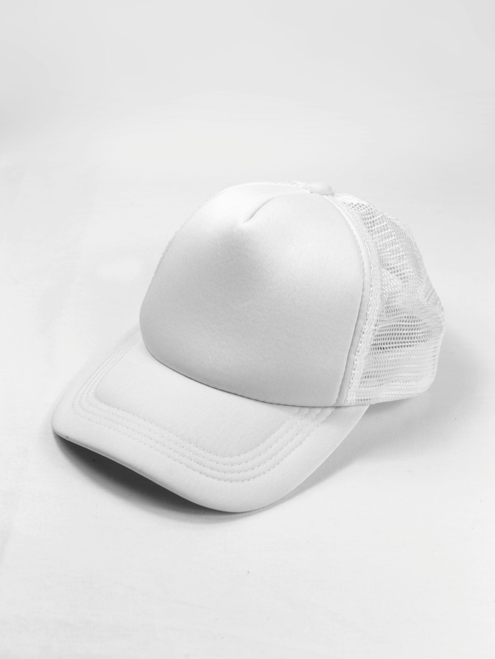 A white trucker hat is sitting on a white surface.
