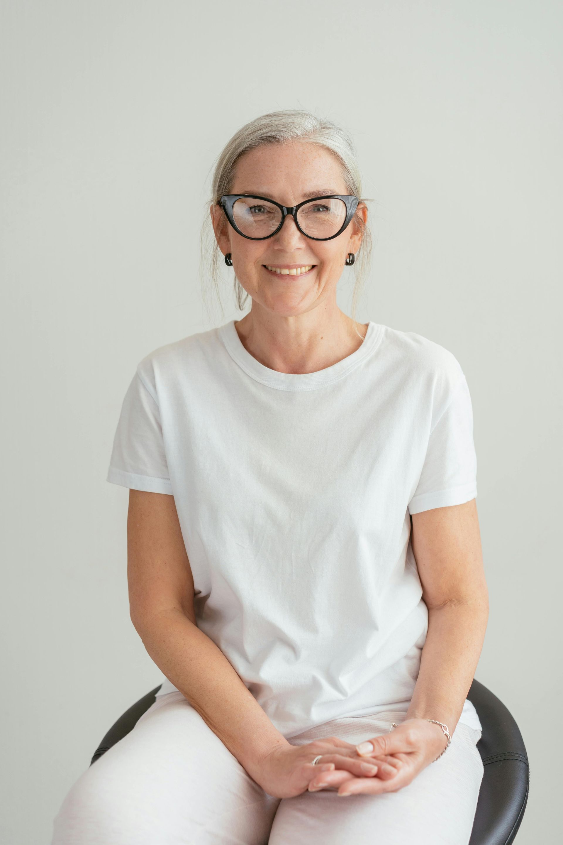 A woman wearing glasses and a white shirt is sitting on a chair.