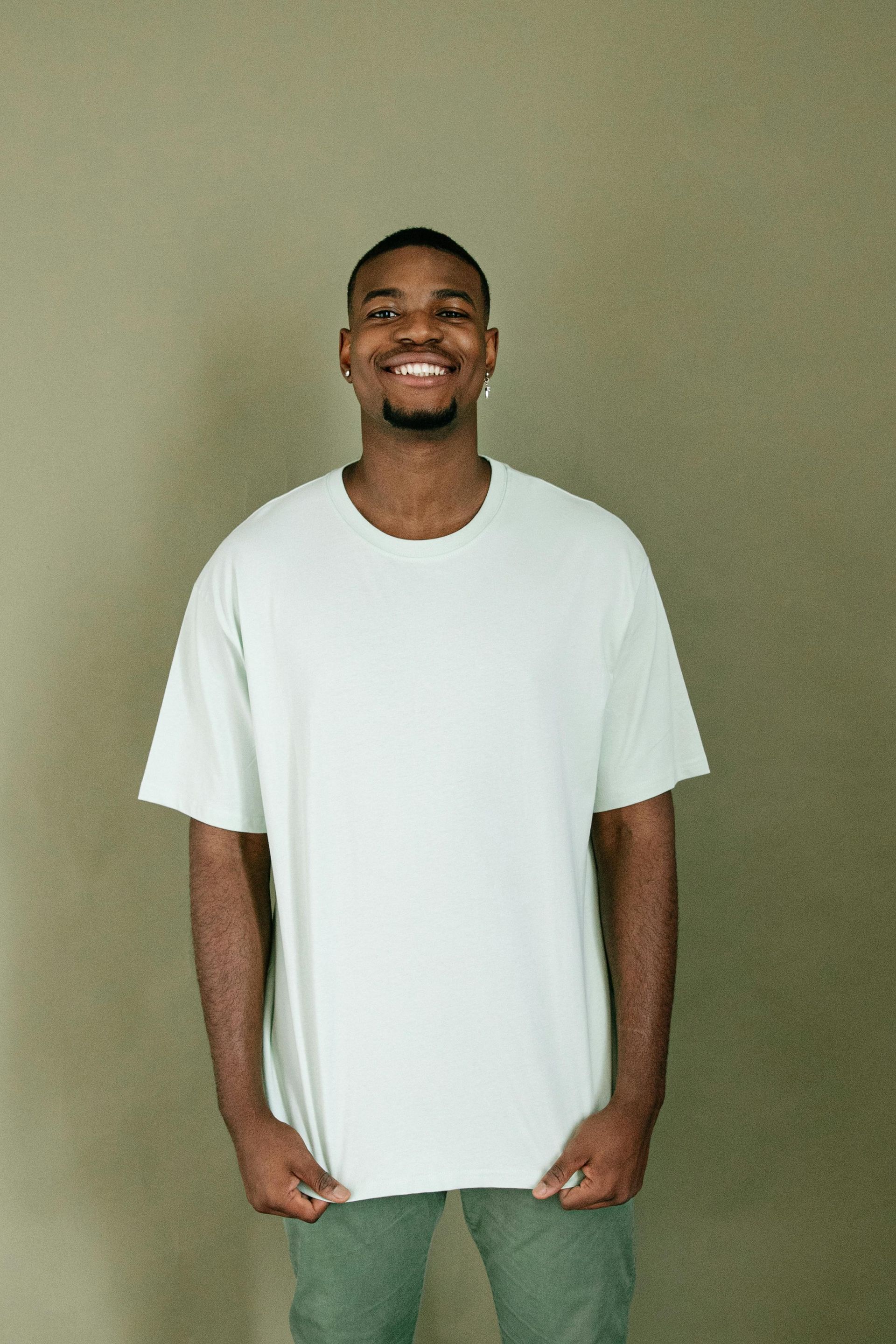 A man wearing a white t-shirt and green jeans is smiling.