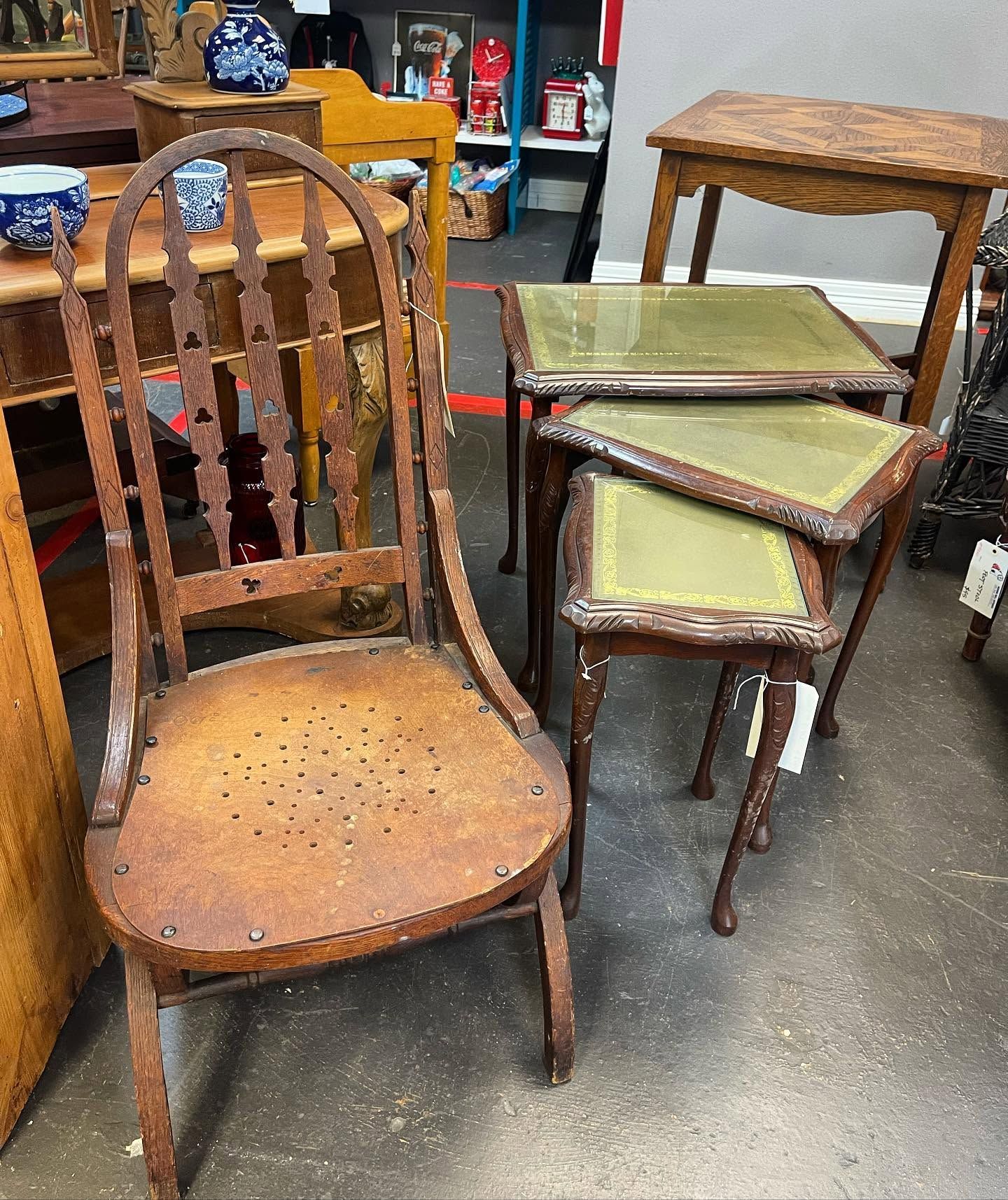 Several vintage wooden chairs and small tables in a workshop or antique shop.
