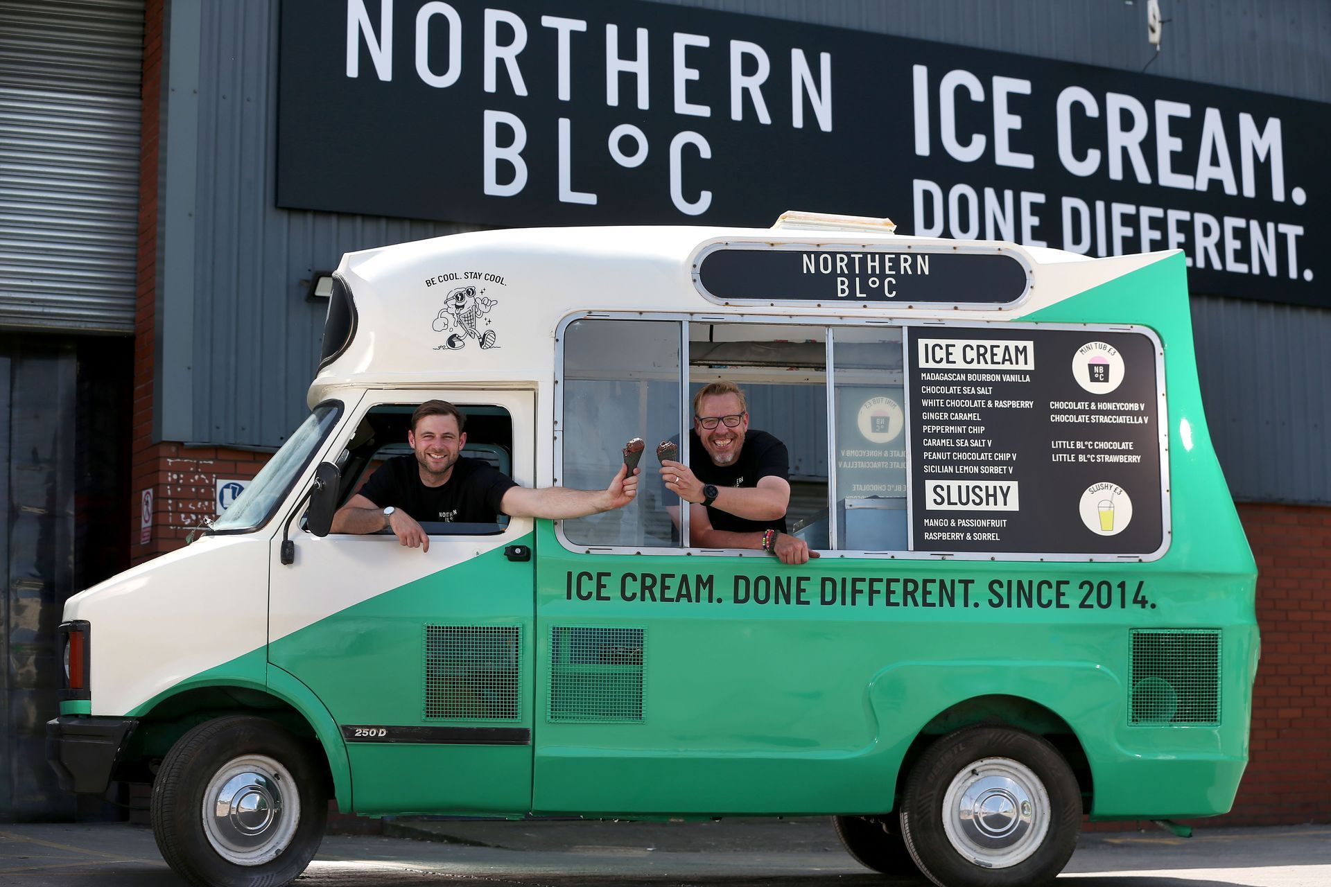 A man in a yellow jacket is talking to another man in a warehouse.