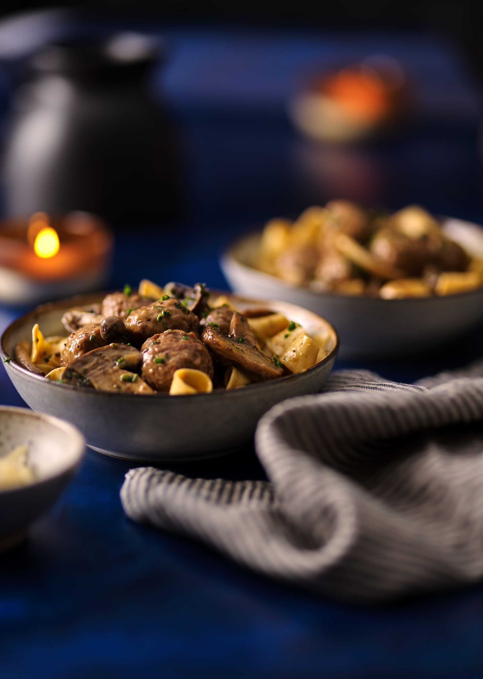Three bowls of food are on a table with a candle in the background.