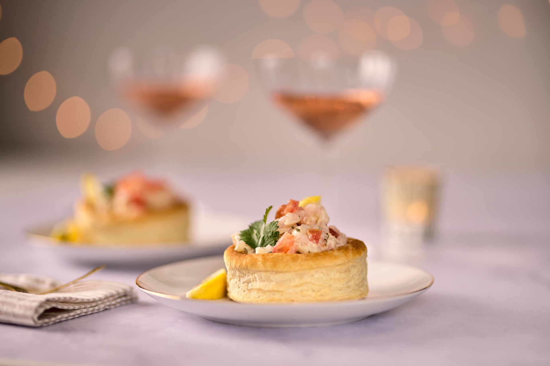 A close up of a plate of food on a table with a glass of wine in the background.