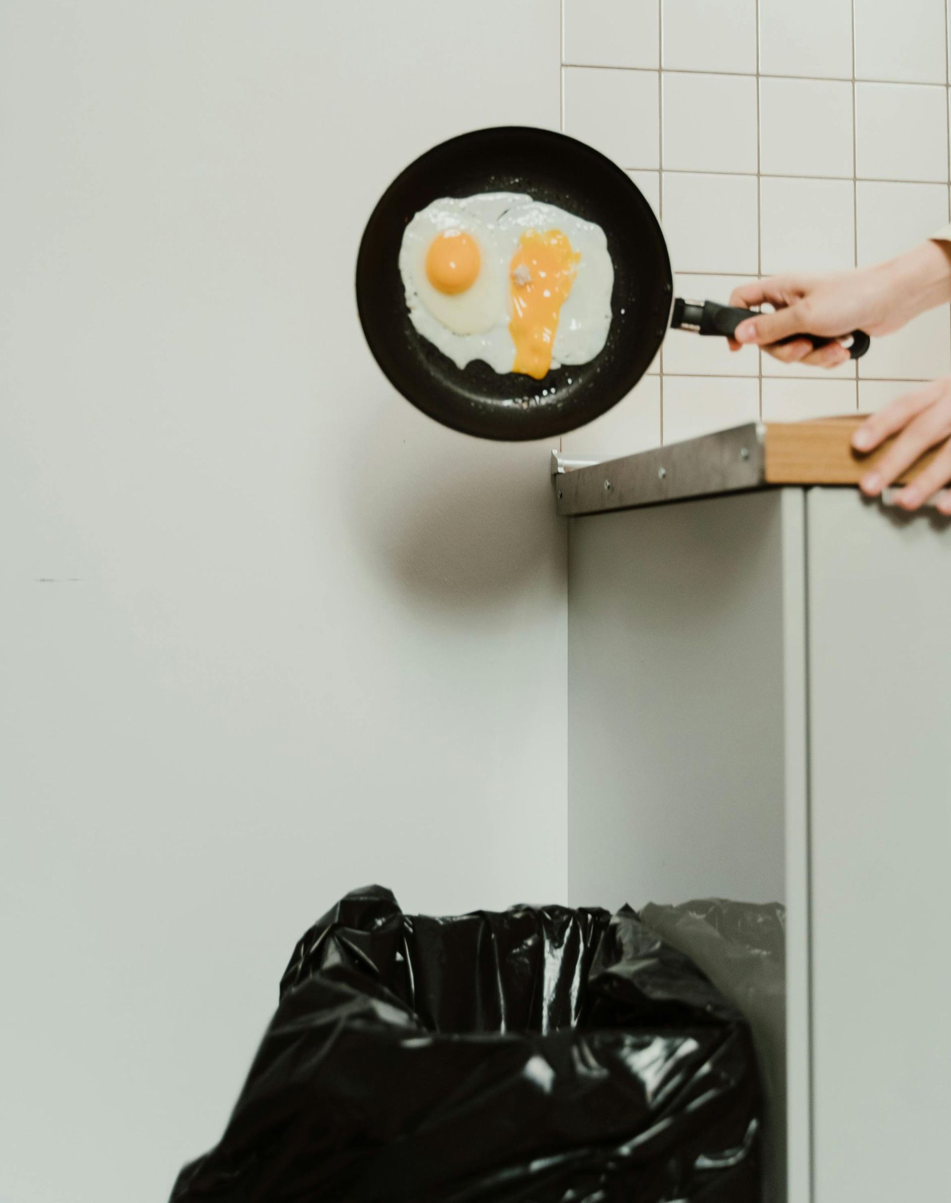 A person is throwing eggs into a trash bag