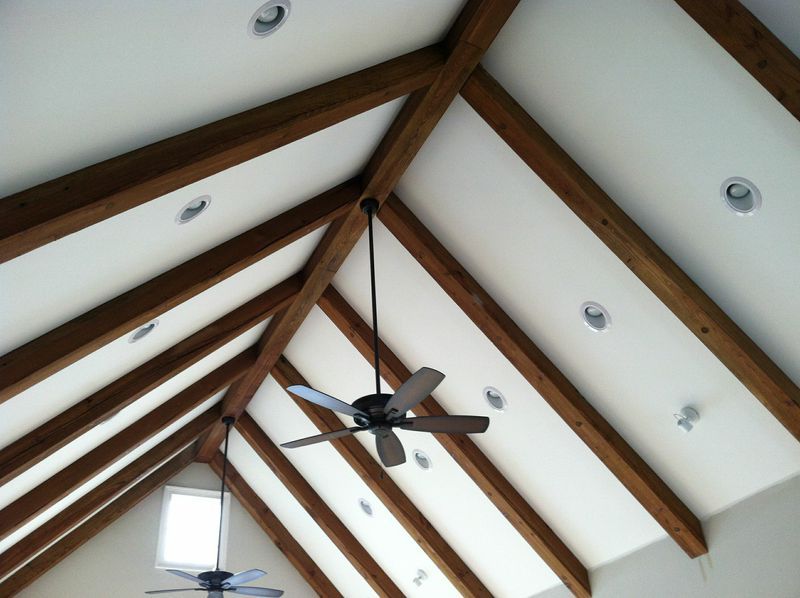 Angled, wood-beamed ceiling with recessed lights and two ceiling fans. White walls and brown beams.