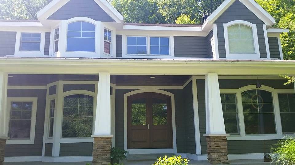 Green house with white trim, columns, and dark wood double doors.