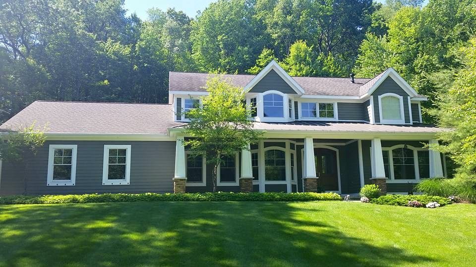 Dark gray house with white trim, green lawn, and trees in the background on a sunny day.