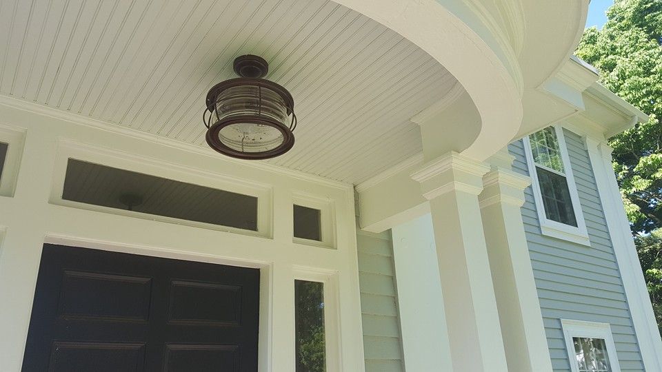 Close-up of a house porch with a decorative lantern, white pillars, and light blue siding.