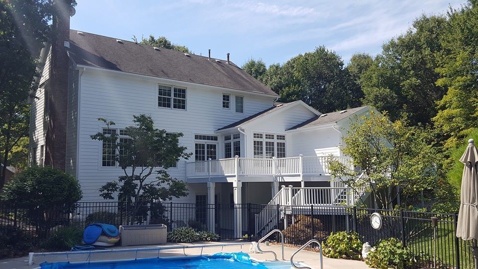White house with a pool. Backyard with a deck and trees on a sunny day.