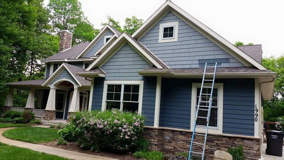 Two-story blue house with a ladder leaned against the side; trim is off-white, with stone foundation and porch.