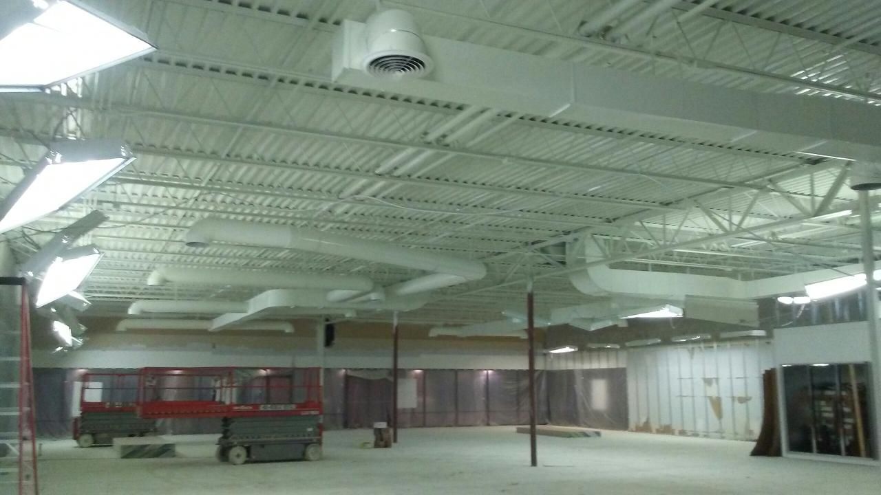Interior of a large commercial space under construction, showing the ceiling with HVAC ducts and unfinished walls.