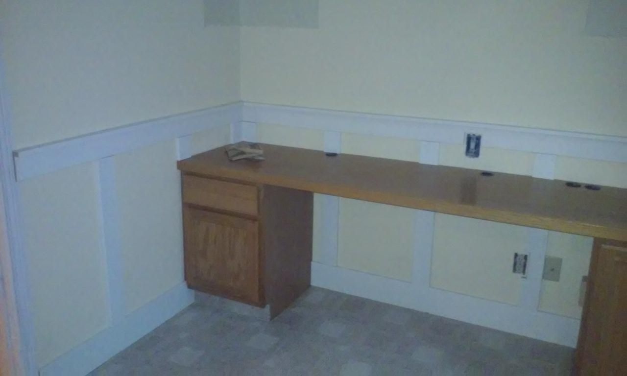 Built-in wooden desk in a corner of a room with light-colored walls and paneling.