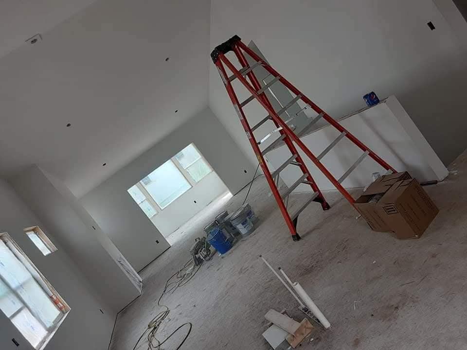 Interior of a room under construction with a ladder. Walls and ceiling are white, floor is gray.