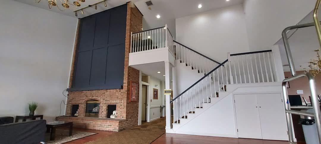 Spacious interior with exposed brick fireplace, staircase, and second-story balcony.