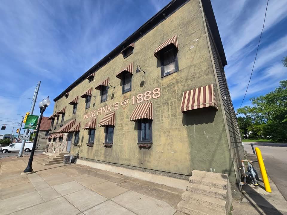 Old brick building with awnings, "Eagle Park" text, street view with sidewalk, blue sky.