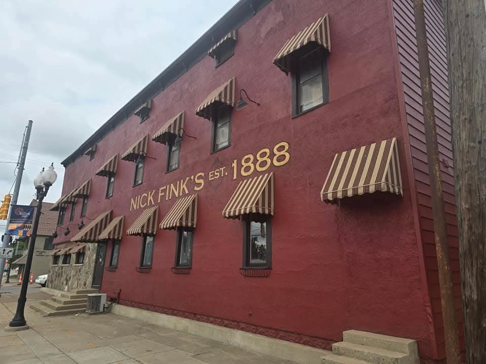 Red brick building, Nick Fink's Est. 1888, with striped awnings over windows. Exterior view, overcast day.