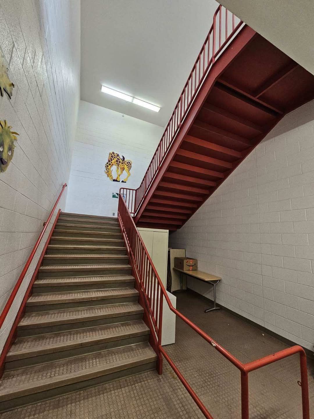 Staircase with red railing in a building; steps lead up, with a landing and continuing upward.