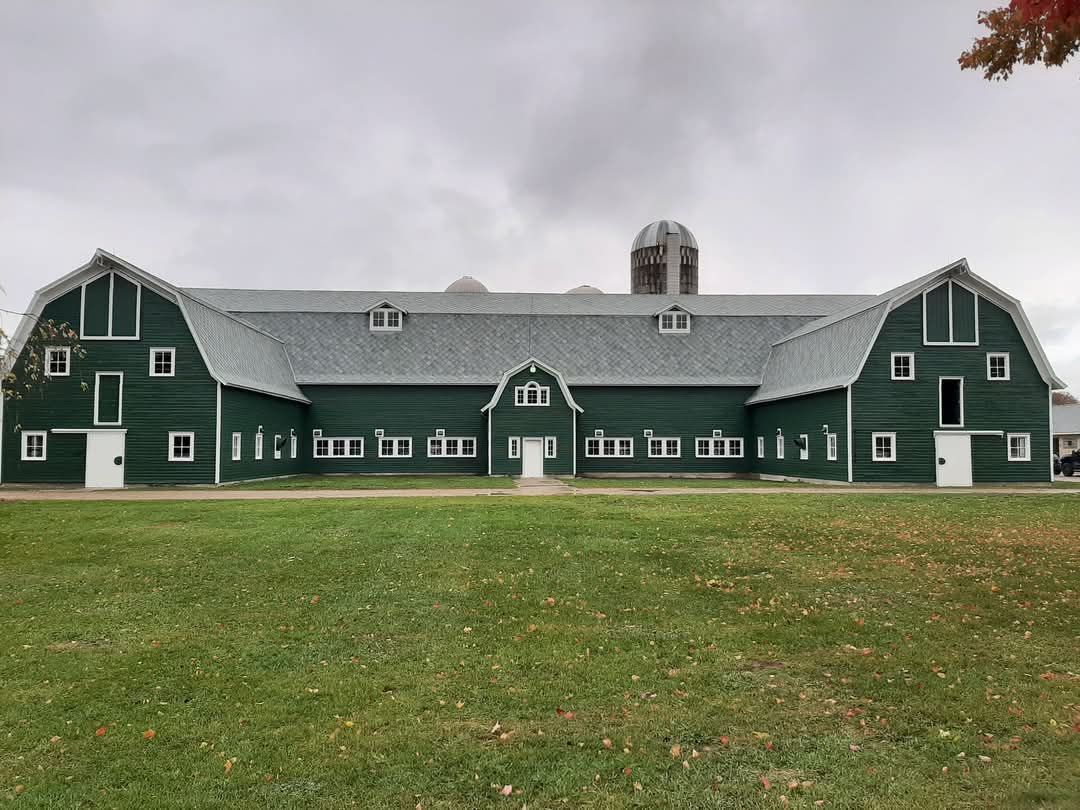 Green barn with white trim under cloudy sky, on a grassy field.