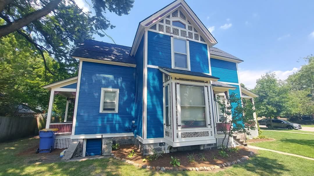 Blue Victorian house with white trim, porch, and bay window under a blue sky.