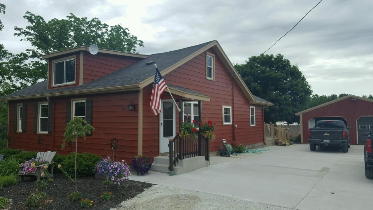 Red house with American flag, black truck in driveway. Overcast day, small garden.