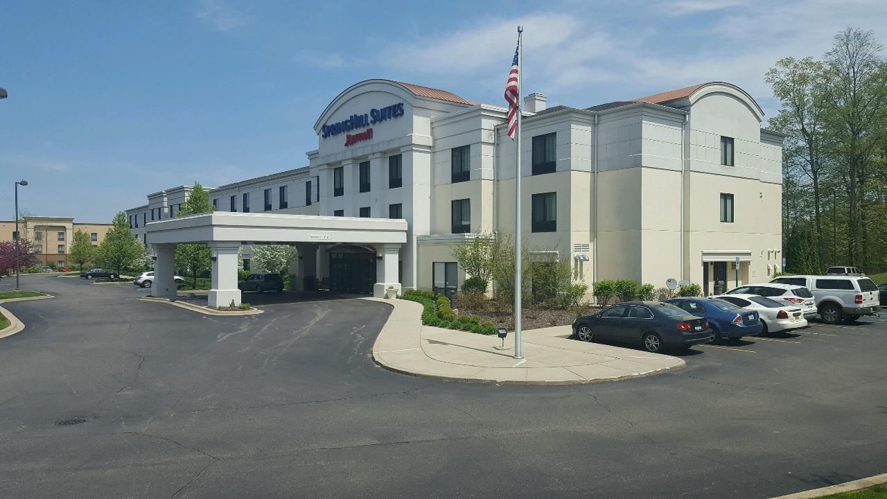 Exterior view of the SpringHill Suites by Marriott. White building with a covered entrance, cars parked in the lot. American flag.