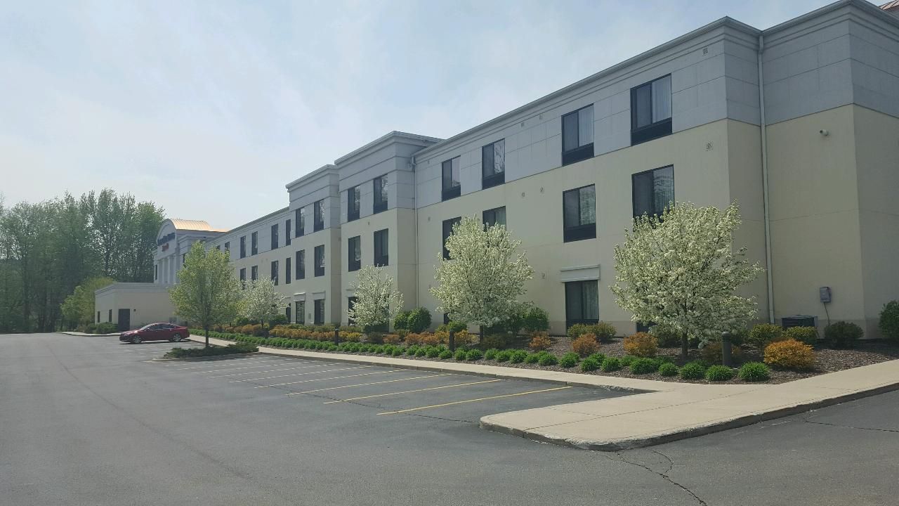 Hotel exterior on a sunny day, with a parking lot and trees in front.