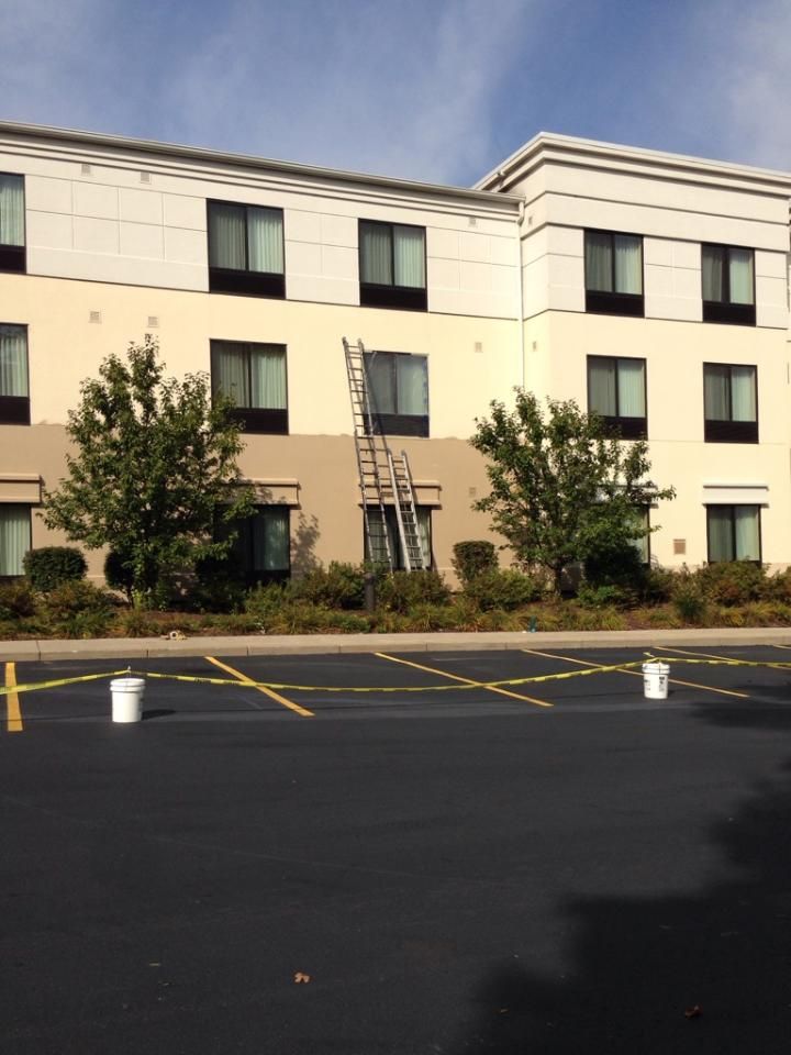 Exterior view of a multi-story building being painted. A ladder leans against the wall; paint buckets sit on the ground.