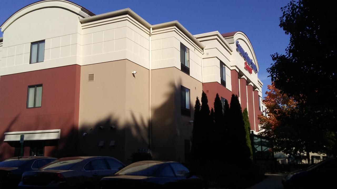 Hotel exterior with red, tan, and white walls. Cars are parked out front. Trees frame the building.