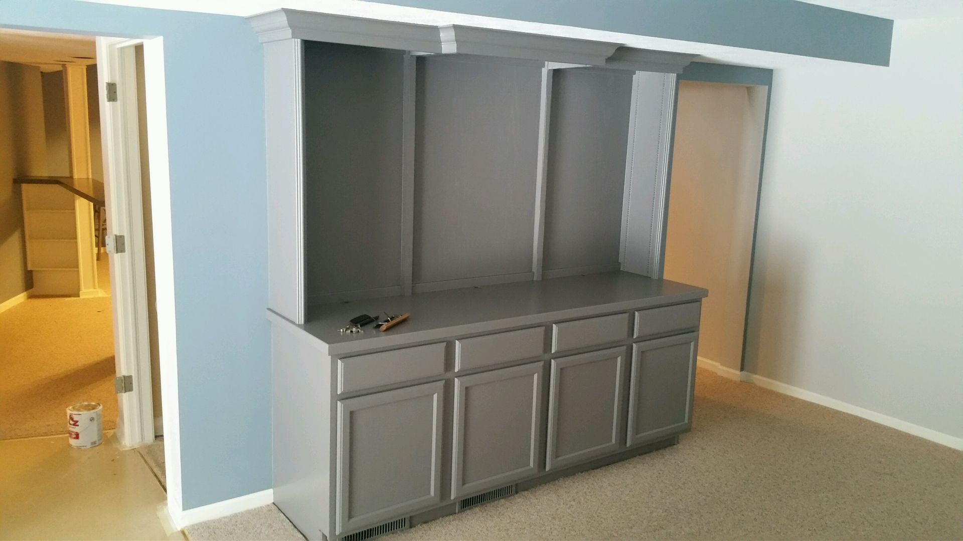 Gray built-in cabinet with upper shelves against blue and white walls, room with beige carpet.