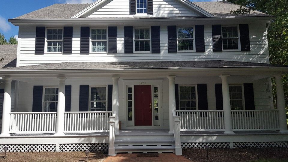 White two-story house with black shutters, red front door, and porch with white columns.